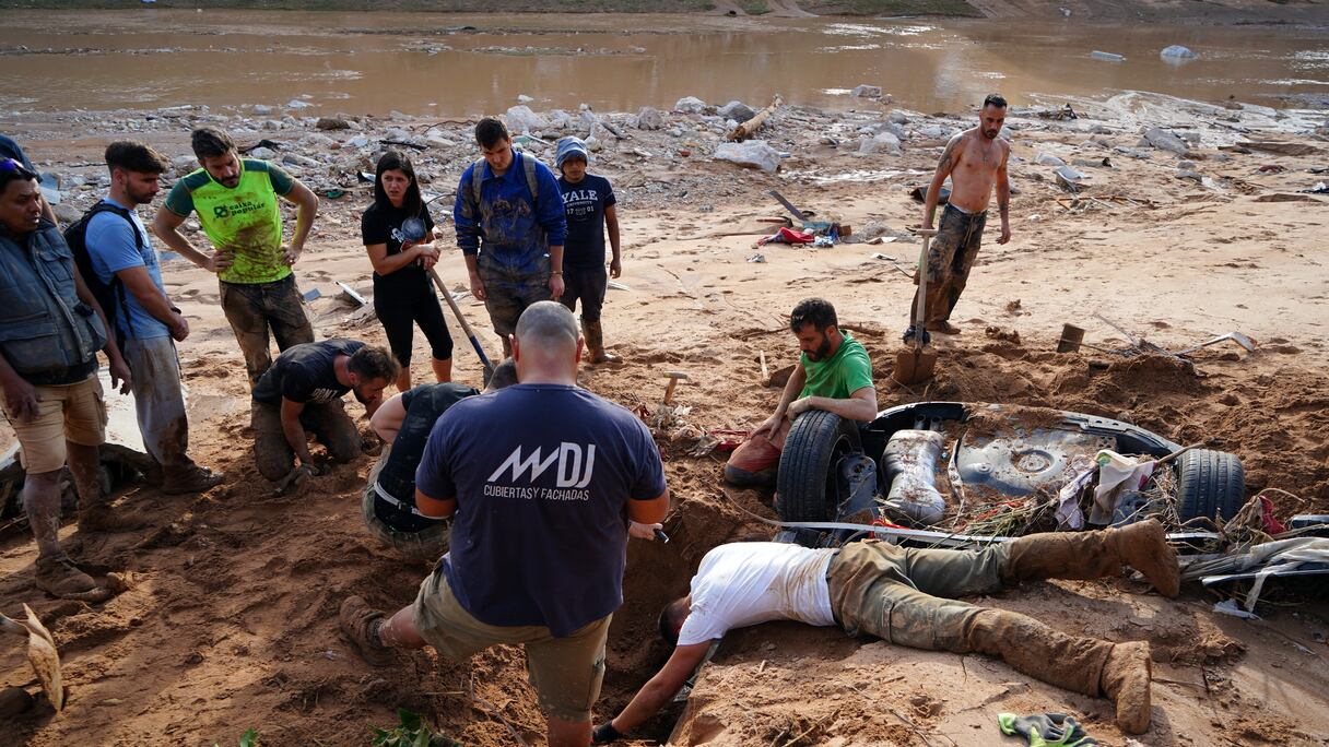 Un groupe de personnes tente de déterrer une voiture à la recherche de victimes enterrées au bord de la rivière, le 1er novembre 2024, après qu'une inondation a dévasté la ville de Paiporta, dans la région de Valence, dans l'est de l'Espagne.